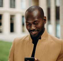 Selective Focus Photo of Smiling Man Looking at His Phone While Holding Cup